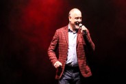 Na scenie SCK Bytków Krzysztof Pietrek. Piosenkarz ma nasobie dżinsy, białą koszulę i czerwoną…
