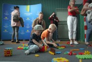 Dzieci układają klocki. W tle ścianka prasowa z logotypami miasta