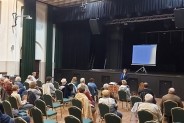 Sala widowiskowa SCK - Bytków z siedzącymi na krzesłach ludźmi zwróconymi ku scenie, na której…