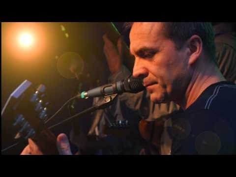 Grający na gitarze muzyk i wokalista Eugeniusz Szwarcer śpiewa do mikrofonu podczas występu.