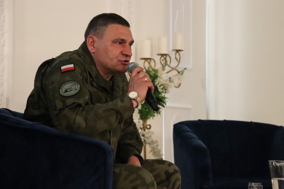 Ireneusz Okoń ubrany w moro z emblematem flagi polskiej na ramieniu trzymajacy mikrofon