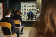 Sala z siedzacymi uczestnikami ,w głębi gość z prowadzącymi spotkanie