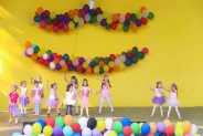 na żółtym tle sceny amfiteatru wiszą kolroowe balony. Na scenie występuje dziecięcy zespół taneczny