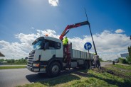 Pojazd z wysięgnikiem oraz pracownicy budowlani w trakcie montażu słupa oświetleniowego.