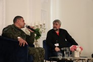 Ireneusz Okoń ubrany w moro z mikrofonem oraz prowadzący w czarnej koszuli siedzą przy stoliku