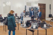 Kobieta w zielonej kurtce przygląda się wystawionym komputerom.