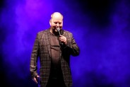 Na scenie SCK Bytków, pośród niebieskiego światła scenicznego stoi konferansjer - Andrzej Miś mi…