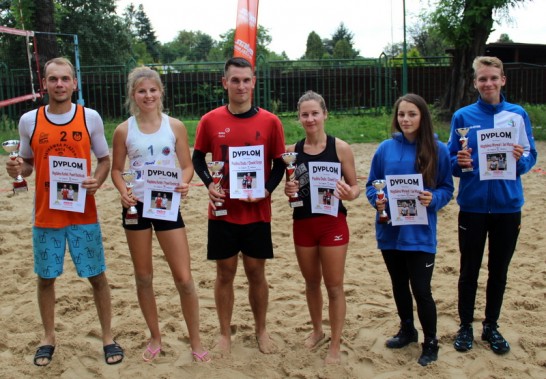 Trzy najlepsze pary Turnieju Siatkówki Plażowej Mixtów stoją na boisku po ceremonii dekoracji…