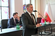 Sekretarz miasta stoi przy mównicy i odpowiada na pytanie radnych