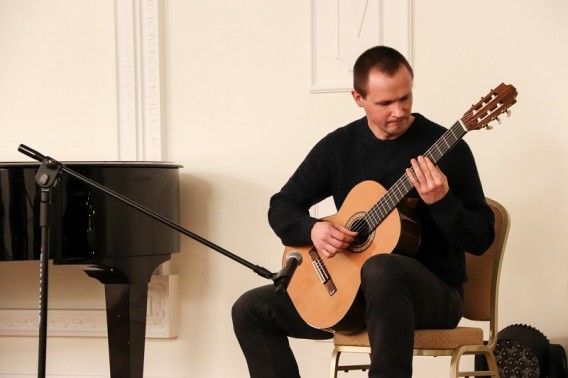 Ubrany na ciemno na krzesie mężczyzna grający na gitarze.