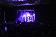 Publiczność widziana od tyłu wraz z artystami na scenie trzymającymi lampiony