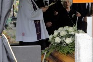 Ksiądz modlący się nad trumną na cmentarzu parafialnym, obok rodzina zmarłego