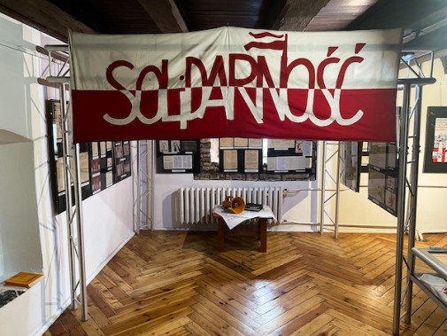 Grafika przedstawia fragment wystawy „13 grudnia roku pamiętnego… Od Solidarności do WRONy”. W…
