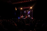 sala widowiskowa SCK Bytków, siedząca publiczność widoczna z tyłu. Oświetlona scena z dwoma muzykami