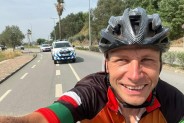 Tomasz Dzierga jadący na rowerze, w tle samochód policyjny.