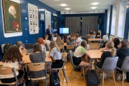 Uczestnicy warsztatów siedzą przy stołach i słuchają wykładowcy.