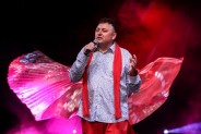 Zbliżenie na postać Wesołego Masorza, ubranego w białą koszulę i czerwone spodnie z szelkami. Za…