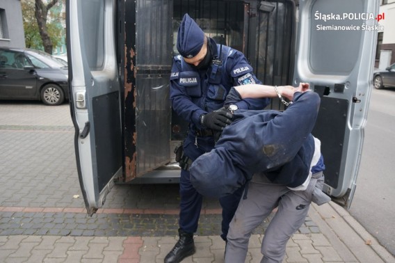 Policjant wyprowadza zatrzymanego z policyjnej furgonetki