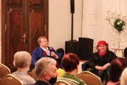 Na tle widzów Piotr Bujoczek z mikrofonem oraz Wanda Bujoczek w strojach ludowych