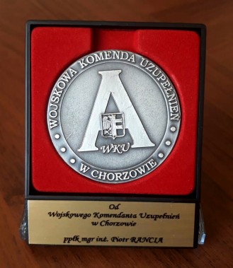 Okrągły srebrny medal z dużą literą A posrodku i logiem Wojskowej Komendy Uzupełnień w Chorzowie…