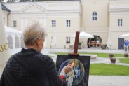 Malarka maluje obraz, w tle budynek Pałacu z bramą wejściową