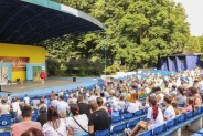 Ogólne zdjęcie z panoramą widowni. Publicznoś siedzi tyłem. W tle scena amfiteatru z widocznym…
