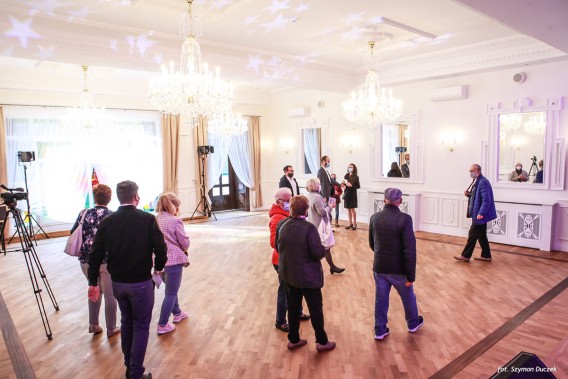 Sala balowa, w środuku grupa zwiedzających ludzi, świecące, kryształowe żyrandole
