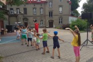 Rząd odwróconych tyłem dzieci, stojących na parkingu, z wyciągniętymi rączkami. W tle tylna…