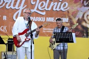 Zbliżenie na Adama Banacha, gitarzystę i wokalistę podczas koncertu w amfiteatrze. Obok niego…