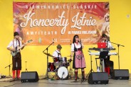 Zespół Tyrolia Band w strojach ludowych gra koncert na tle żółtej ściany amfiteatru i baneru…