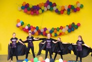 Na żółtym tle sceny amfiteatru wiszą kolorowe balony. Na scenie występuje ubrany na czarno zespół…