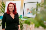 Justyna Ślósarek ubrana w czarną sukienkę na tle swoich prac.