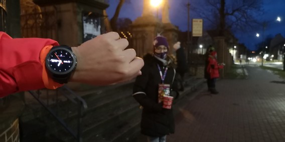 Ręka z zegarkiem wskazującym kwadrans przed siódmą, W głębi wolontariusze.