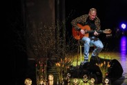Na scenie gra na gitarze Adam Bul. Przed nim dekoracja sceniczna