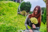 Fotografia: lustrzane odbicie dziewczyny siedzącej na łące z kwiatem w dłoni