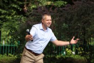 Jacek Krupa w jasnej koszuli i jasnych spodniach prowadzi dialog z widownią. W tle zieleń drzew…
