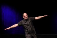 Na scenie ubrany na czarno mim - Ireneusz Krosny. Ma szeroko rozpostarte ręce. Za nim czarne tło