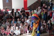 Dzieci siedzą na podłodze. Przed nimi klown