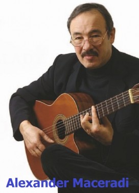 Alexander Maceradi w okularach z gitarą, ubrany w czarny garnitur i czarny golf. Zdjęcie z…