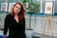 Justyna Ślósarek ubrana w czarną sukienkę na tle swoich prac w oranżerii SCK Zameczek.