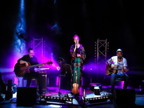 Widok na scenę oświetloną kolorowymi światłami. Na scenie troje muzyków zespołu Mikromusic.…