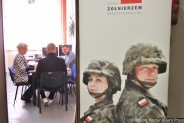 Po lewej członkowie komisji kwalifikacyjnej siedzą za biurkiem. Przed nimi siedzi (odwrócony…