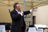 Na pierwszym planie Juliusz Ursyn Niemcewicz ubrany w czarną marynarkę i białą koszulę. W ręce…