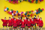 Na żółtym tle sceny amfiteatru wiszą kolorowe balony. Na scenie występuje dziecięcy zespół…