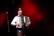 Na scenie akordeonista Grzegorz Wituła podczas koncertu. Ubrany w białą koszulę, gra na…