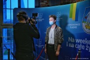 Jakub Lenc pozujący na ściance z logotypami miasta. Przed nim stoi kamerzysta