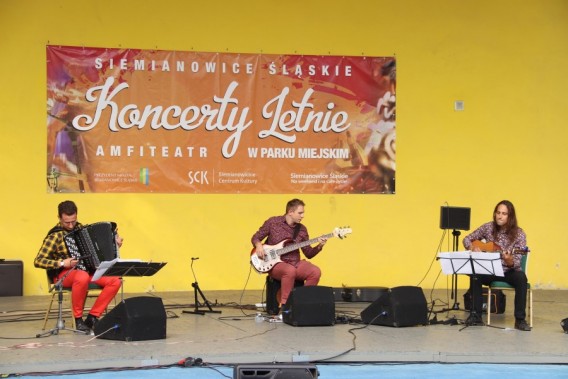 Zespół Nivel na scenie amfiteatru. Trzech muzyków siedzi na scenie na krzesłach i grają na…