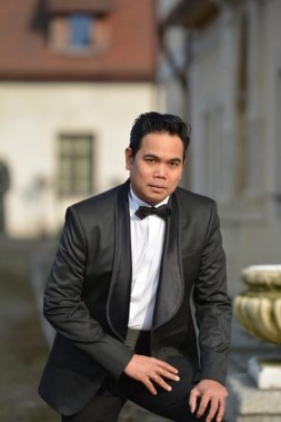 Na zdjęciu Alex Martinez w czarnym stroju galowym stoi na tle kamienic