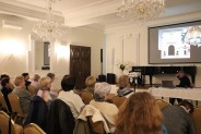 Sala Lustrzana siedząca publiczność za stołem siedzi prelegent na ekranie slajd ze zdjęciami z…