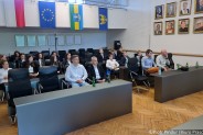 Młodzi sportowcy wraz z trenerami siedzą w dużej sali ratusza